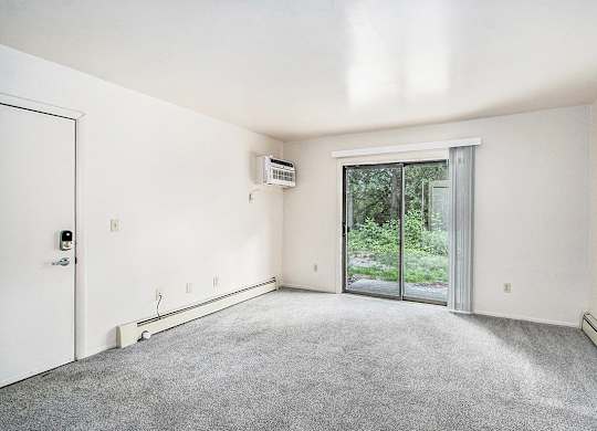 A living room with a carpet floor, a sliding glass door, and a white door at Concord Place Apartments, Kalamazoo, MI