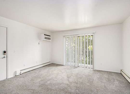 A living room with a sliding glass doors covered by blinds and a carpeted floor at Concord Place Apartments, Kalamazoo, MI