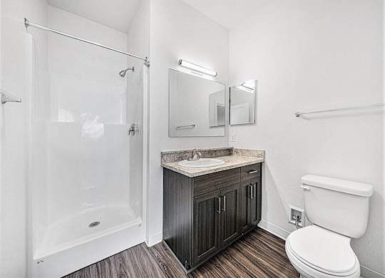 A white toilet sits next to a sink in a bathroom an empty bedroom with a ceiling fan and ensuite at Copper Creek Apartment Homes, Kansas, 67101