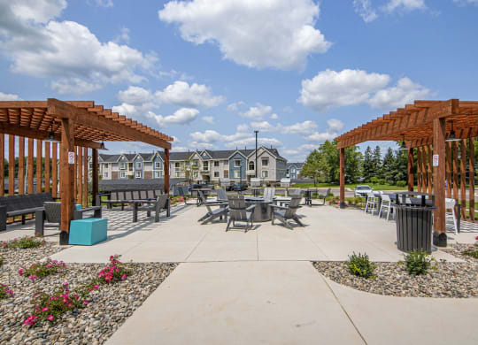 an outdoor pergola with tables and fire pit with seating at The Crossings Apartments, Michigan, 49508