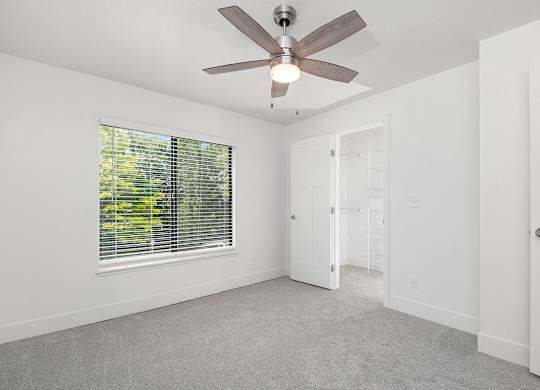 A bedroom with a ceiling fan and a window with blinds at The Crossings Apartments, Grand Rapids, Michigan