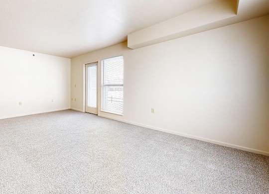 An enlarged living room with a carpeted floor and a door leading to a patio at Dupont Lakes Apartments, Fort Wayne
