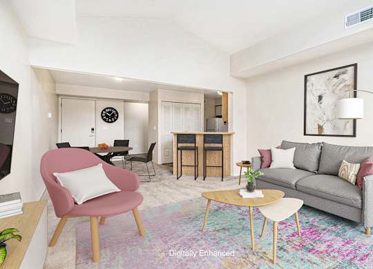 A living room with a cathedral ceiling, grey couch, a pink chair, and a wooden coffee table at Dupont Lakes Apartments, Fort Wayne