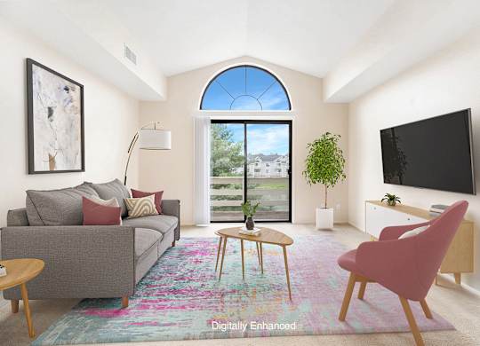 A living room with a grey couch, a pink chair, a small table, a flat screen TV, and a large window with a view at Dupont Lakes Apartments, Fort Wayne