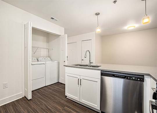 A modern kitchen with a stainless steel dishwasher and white cabinets and a full size washer and dryer at Eagle Ridge Apartment Homes, Traverse City, MI 49685