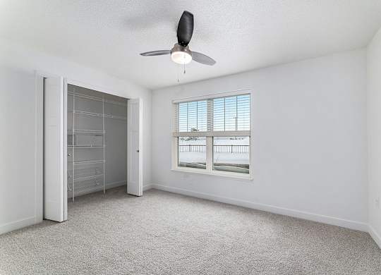 A spacious bedroom with a ceiling fan and large windows and a walk in closet with organizers at Eagle Ridge Apartment Homes, Traverse City, MI 49685