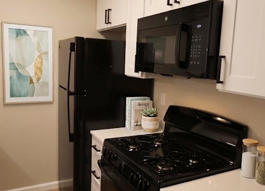 A black refrigerator and microwave in a kitchen with white cabinets.