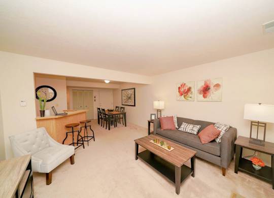 A living room with a couch, a chair, a coffee table, and a dining table at Emerald Park Apartments in Kalamazoo, MI