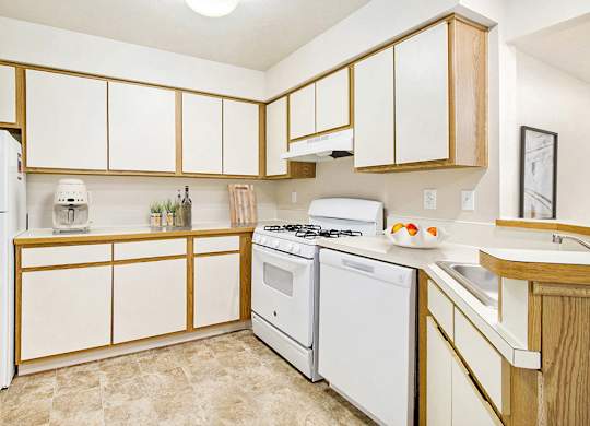 A kitchen with white appliances and wooden cabinets at Emerald Park Apartments, Kalamazoo, Michigan