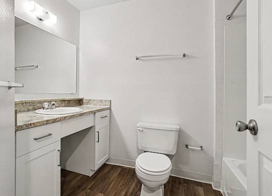 A white bathroom with a toilet, sink, and mirror at Emerald Park Apartments, Kalamazoo, Michigan
