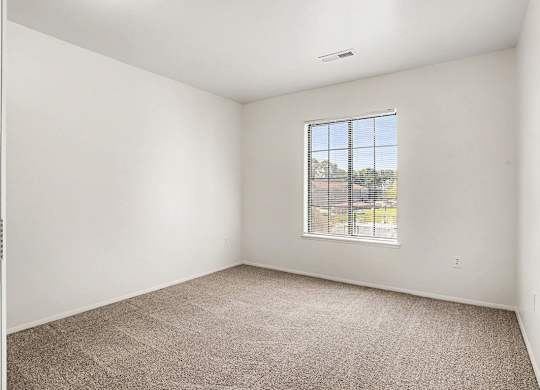 A bedroom with a carpeted floor and a large window at Emerald Park Apartments, Kalamazoo, Michigan
