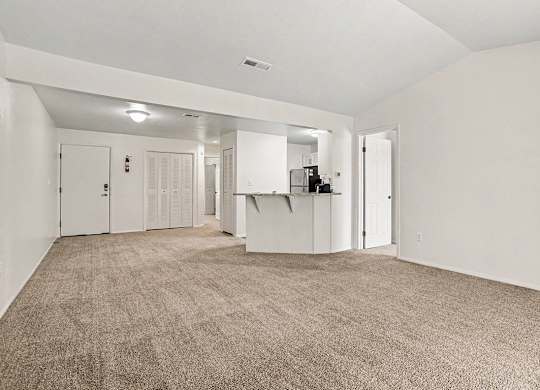 A large, empty living room with carpeted flooring and white walls at Emerald Park Apartments, Kalamazoo, Michigan