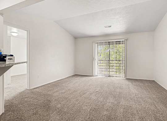A living room with a carpeted floor and a sliding glass door to a balcony at Emerald Park Apartments, Kalamazoo, Michigan