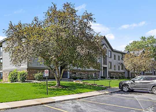 A tree in front of an apartment building with green grass at Emerald Park Apartments in Kalamazoo, MI