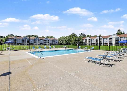 A swimming pool surrounded by chairs and apartment buildings in the background at Emerald Park Apartments in Kalamazoo, MI