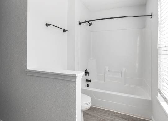 a white bathroom with a tub and a toilet and a window at Latitudes Apartments, Indianapolis, IN, 46237
