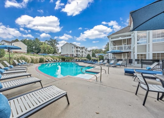 a resort style pool with lounge chairs and umbrellas in front of a building at The Vinings Apartments in Richmond, VA