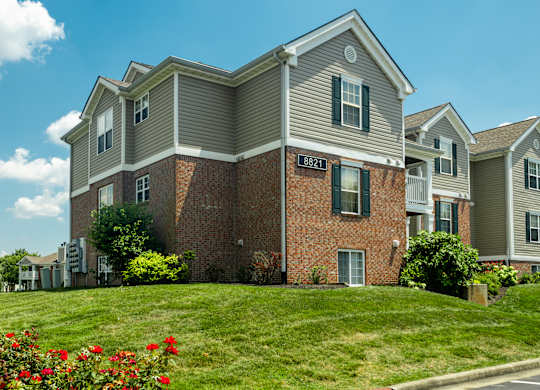 Apartment building with a red brick wall and a green lawn in front.