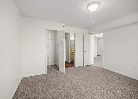 A white bedroom with a carpeted floor and an ensuite bathroom with a walk-in shower  at West Hampton Park Apartment Homes, Nebraska, 68022