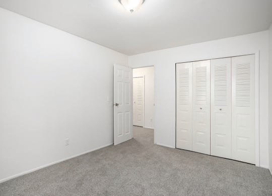 an empty bedroom with white closets and carpeting at Fairlane Apartments in Springfield, MI