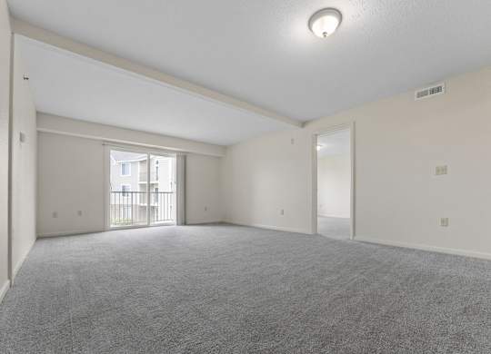 A spacious living room with a carpeted floor and a sliding glass door to a balcony at Fieldstream Apartment Homes in IA 50023