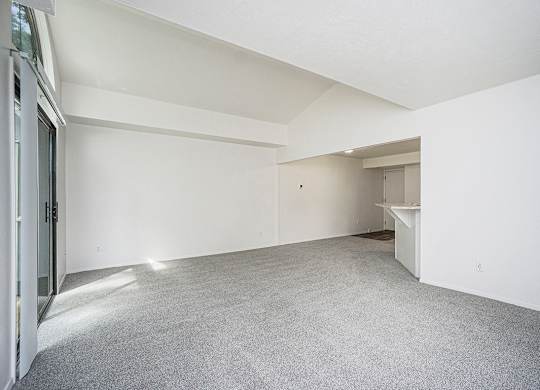 A large, empty living room with white walls and a grey carpet at Foxwood and The Hermitage in Portage, MI