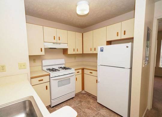 A two bedroom kitchen with a white refrigerator, stove, and sink at Foxwood and The Hermitage, Portage, MI