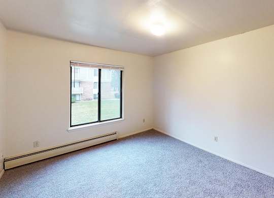 A large bedroom with a window and a carpeted floor at Glen Oaks Apartments, Michigan, 49442