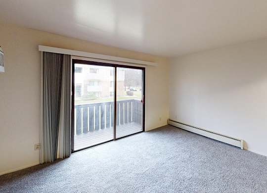 A living room with carpeting and a sliding glass door at Glen Oaks Apartments, Michigan, 49442
