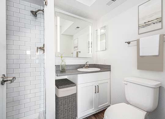A white toilet is in a bathroom with a white tiled shower at Green Ridge Apartments, Grand Rapids, MI