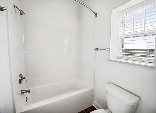 A white bathroom with a toilet and a bathtub at The Grove Apartment Homes in Lincoln, NE