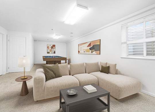 A basement recreation room with a beige couch, a coffee table, and a lamp at Gull Prairie/Gull Run Apartments and Townhomes, Michigan