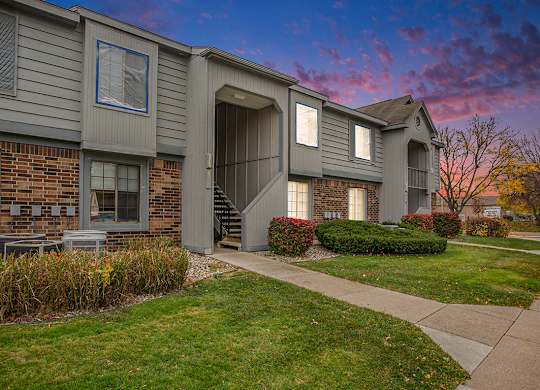 A grey building with a brick wall and landscaping in front at Hampton Lakes Apartments, Walker, 49534