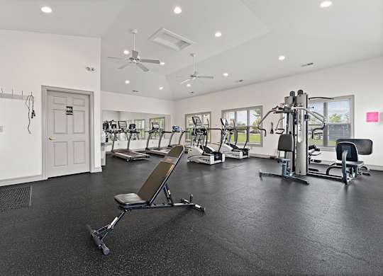 A spacious gym with a variety of equipment including a treadmill, a stationary bike, a rowing machine, and a weight bench at Hunters Pond Apartment Homes, Illinois, 61820
