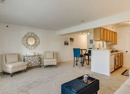 A living room with a white couch, two chairs, a coffee table, and a kitchen area in the background  at Northport Apartments, Macomb, MI, 48044