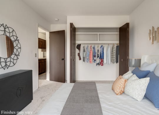 a bedroom with a large bed and a closet with clothes hanging on the wall at The Landings Apartments, Westland, MI