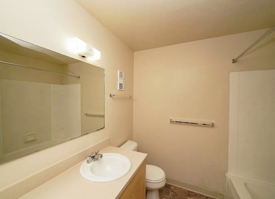 A bathroom with a toilet, sink, and mirror at Irish Hills Apartments, South Bend, IN