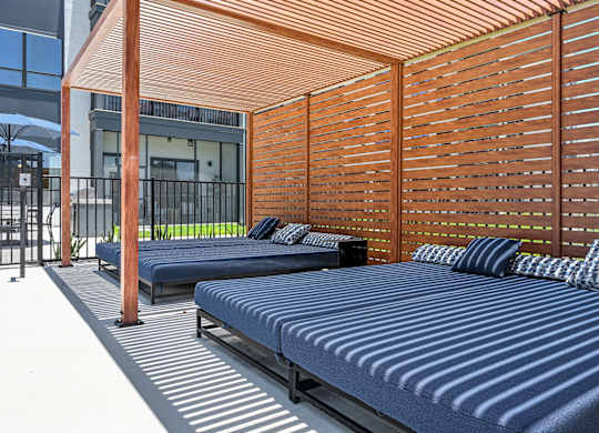 A wooden pergola with a striped bed underneath it at Ironwood Flats Apartments, Florida