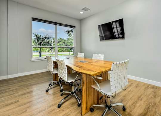 A conference room with a wooden table and chairs, a flat screen TV on the wall, and a window with a view of the outdoors at Ironwood Flats Apartments, Brandon