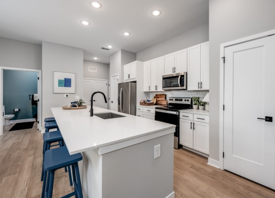 a kitchen with white cabinetry and a large white island with a sink and three stools at Ironwood Flats, Brandon, Florida