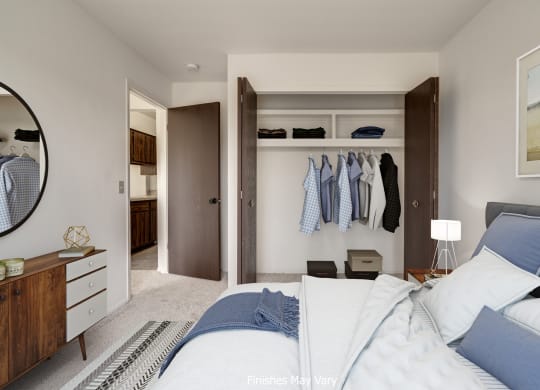 a bedroom with a large bed and a closet with clothes hanging on the wall at The Landings Apartments, Westland