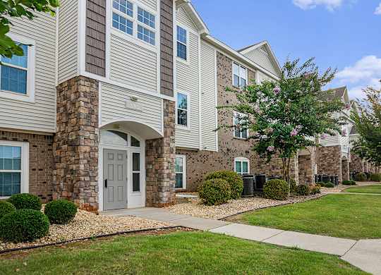 An exterior apartment building with a white door and windows with bushes in front at Limestone Creek Apartment Homes, Madison, AL