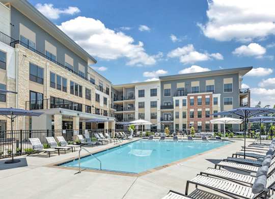 A large swimming pool surrounded by sun loungers and umbrellas in front of apartment buildings at Luxe 360 on Centerpointe Apartments, Midlothian