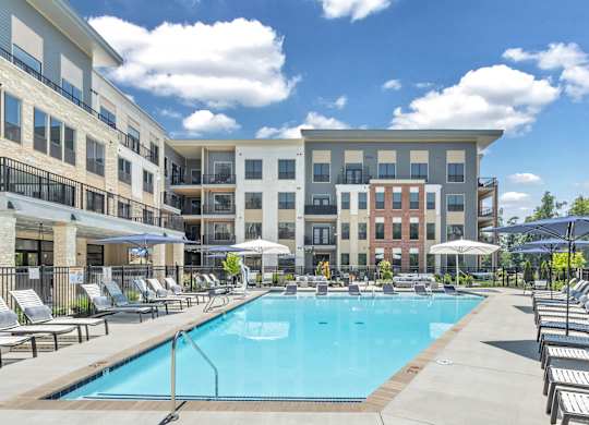 A large swimming pool surrounded by sun loungers and umbrellas in front of a multi-story apartment building at Luxe 360 on Centerpointe Apartments, Midlothian, Virginia