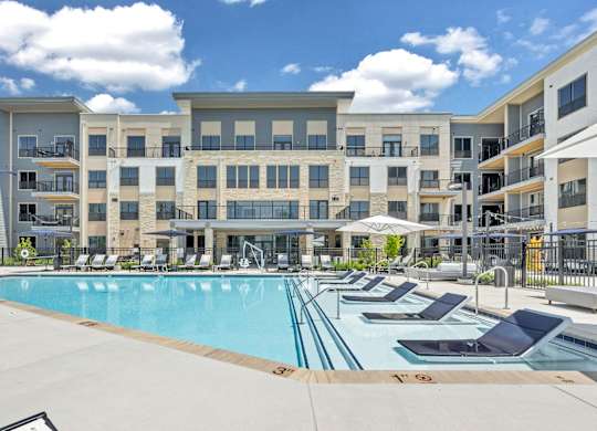A large swimming pool surrounded by sun loungers in front of apartment buildings at Luxe 360 on Centerpointe Apartments, Virginia, 23114