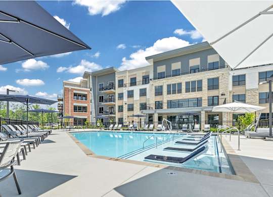 A large swimming pool is surrounded by sun loungers and umbrellas at Luxe 360 on Centerpointe Apartments, Virginia