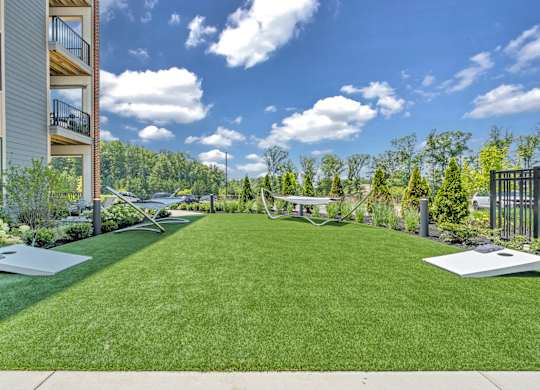 A large grassy area in front of a building with a white lawn chair and a black metal fence at Luxe 360 on Centerpointe Apartments, Midlothian, 23114