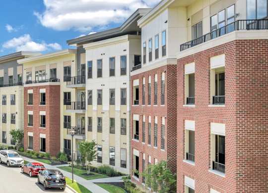 A row of red brick apartment buildings with cars parked in front at Luxe 360 on Centerpointe Apartments, Midlothian, Virginia
