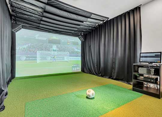 A soccer ball is on a green mat in front of a screen showing a soccer game at Luxe 360 on Centerpointe Apartments, Virginia, 23114