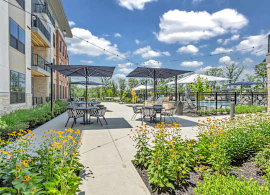 A patio with tables and chairs is surrounded by plants and flowers at Luxe 360 on Centerpointe Apartments, Midlothian, Virginia